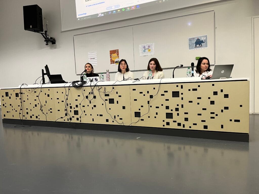 Photo prise lors d'une conférence, quatre personnes assises derrière un grand bureau dans un amphithéâtre