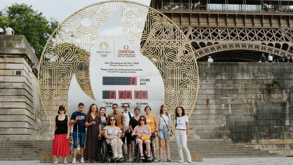 Photo d'un groupe de personnes devant un monument des Jeux Olympiques de Paris 2024, on voit la Tour Eiffel en arrière-plan