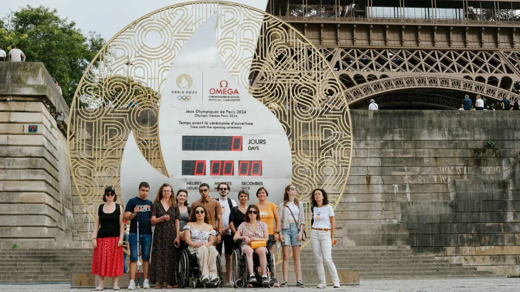 Photo d'un groupe de personnes devant un monument des Jeux Olympiques de Paris 2024, on voit la Tour Eiffel en arrière-plan